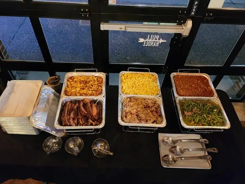 Trays of smoked BBQ and sides set up for a catered event
