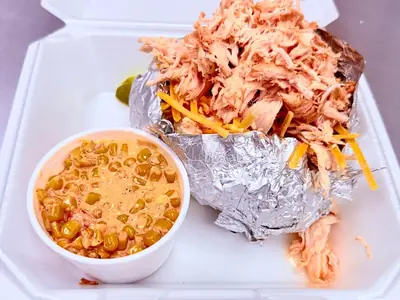 Loaded baked potato piled with smoked pulled chicken and cheddar, with cheesy cream corn