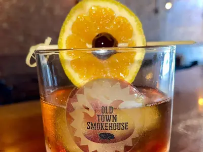 A Perfect Old Fashion with an orange wheel and cherry in an Old Town Smokehouse rocks glass